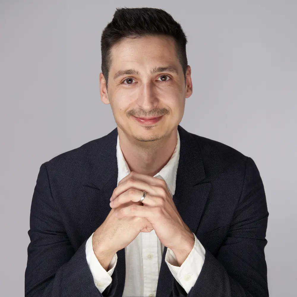 Andrei leaning slightly forward, hands together, looking into the camera.